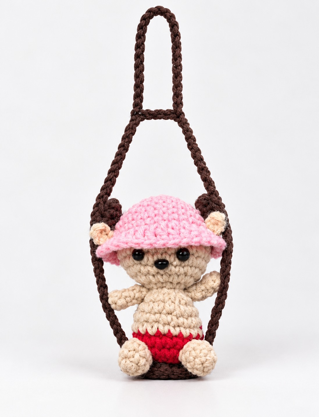 Beige crochet bear wearing a pink hat on a brown swing