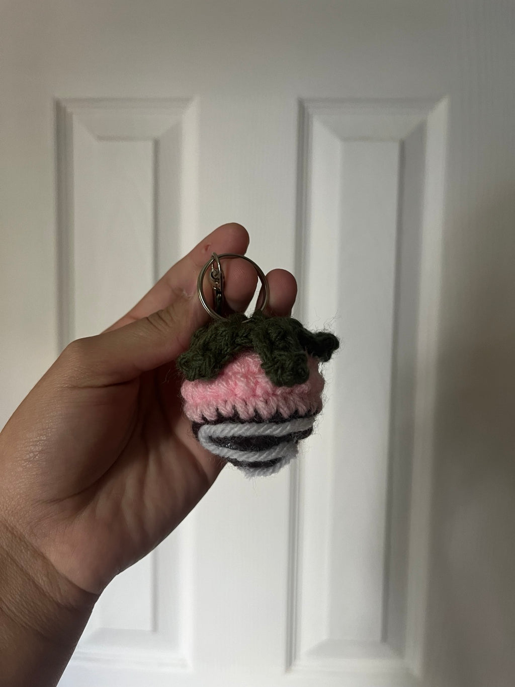 Pink crochet strawberry dipped in dark chocolate with white stripes and green leaves.