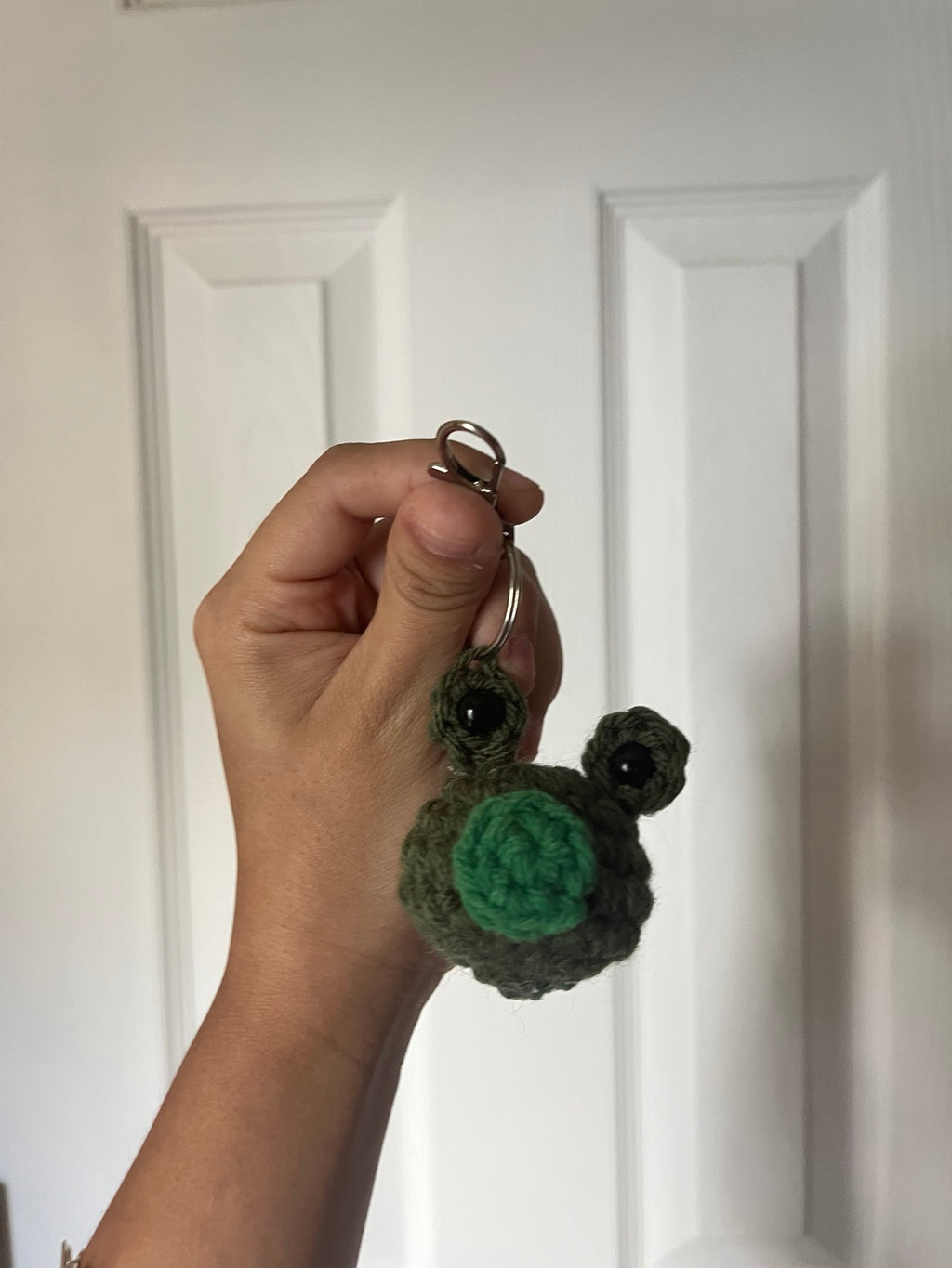 Green crochet frog face with raised eyes on a keyring.