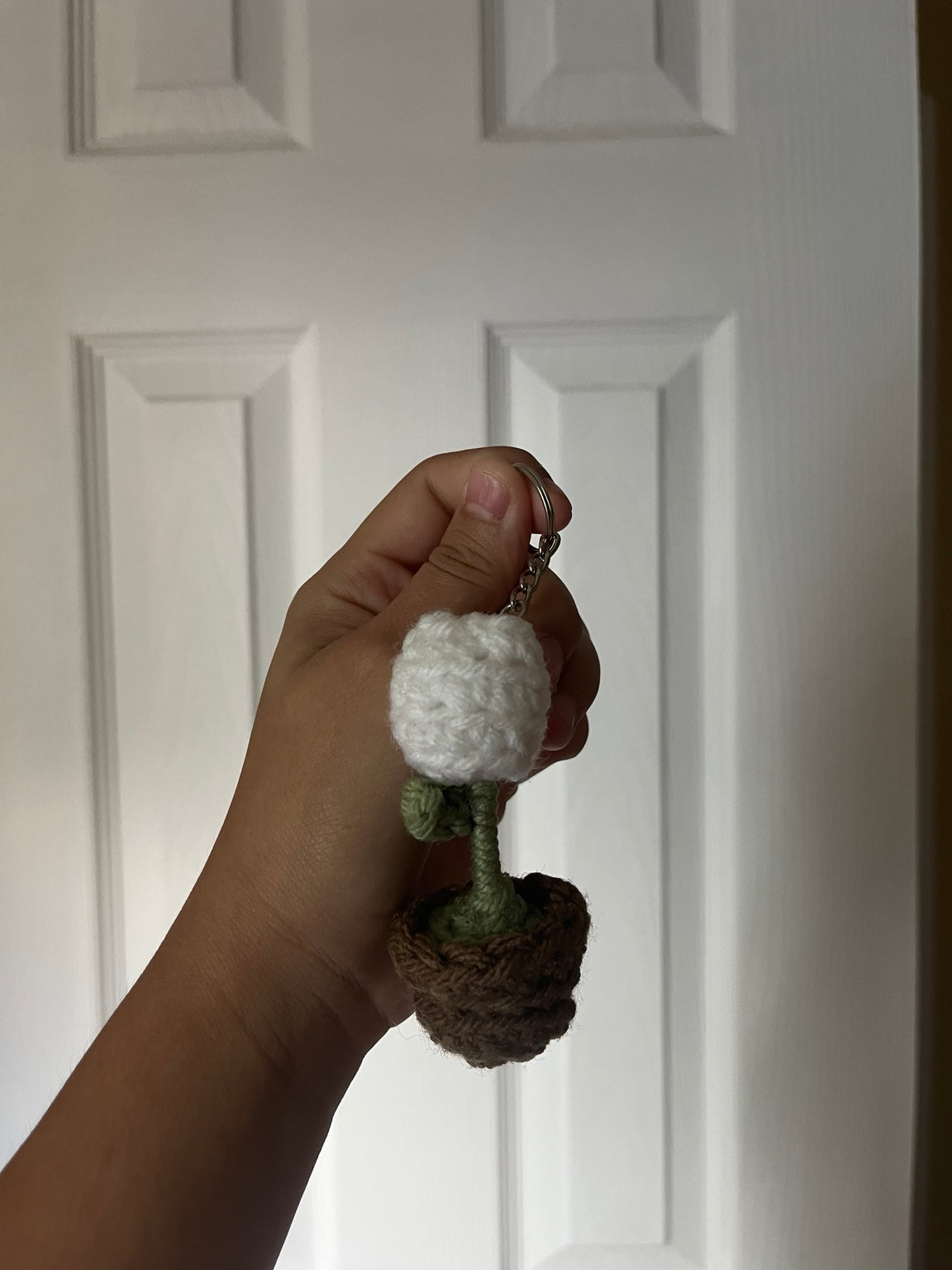 A white crochet flower on a green stem in a brown pot.