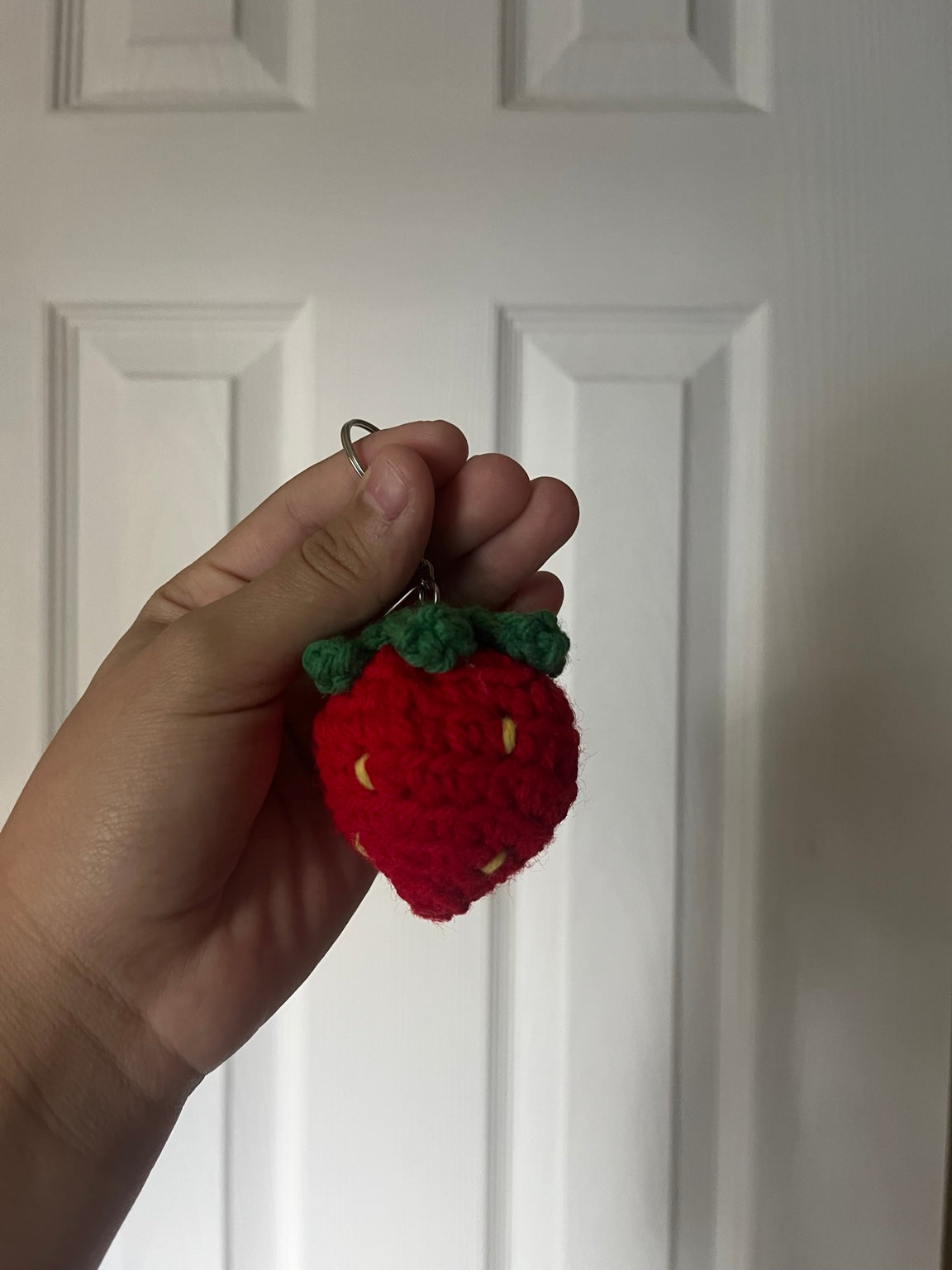 Red crochet strawberry with green leaves and yellow seeds.